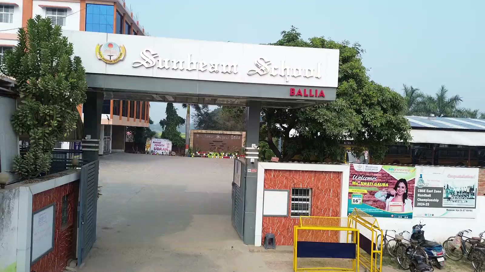 The entrance of Sunbeam School Ballia: the school’s name in raised lettering across the archway beside the crest, with the drive running in past the school sign to the buildings beyond.